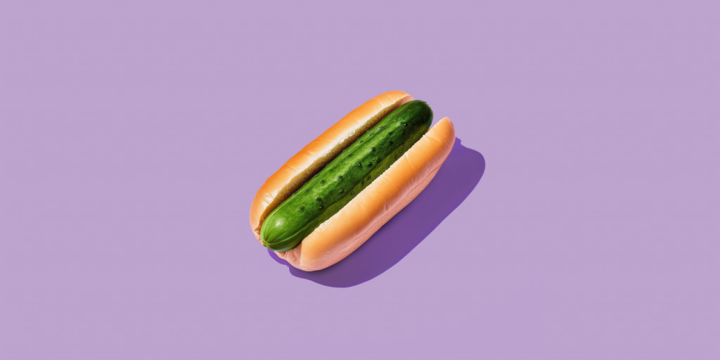 Foto einer Gurke in einem Hot Dog Brötchen auf lila Untergrund